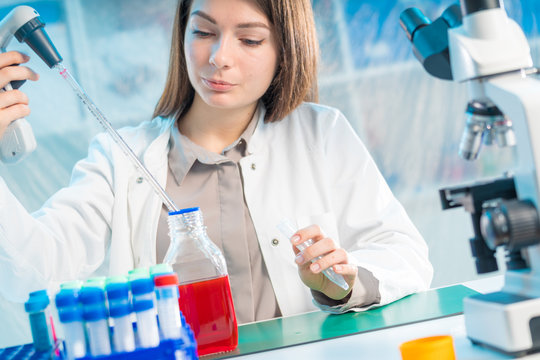 Young woman in scientific lab with pipette and chemicals in test tubes