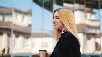 Young transgender woman walks with a cup of coffee along the mirror wall outside - Powered by Adobe
