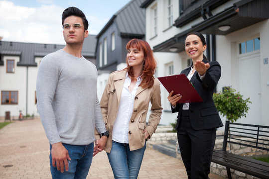 Young couple with real estate agent visiting house for sale in residential area