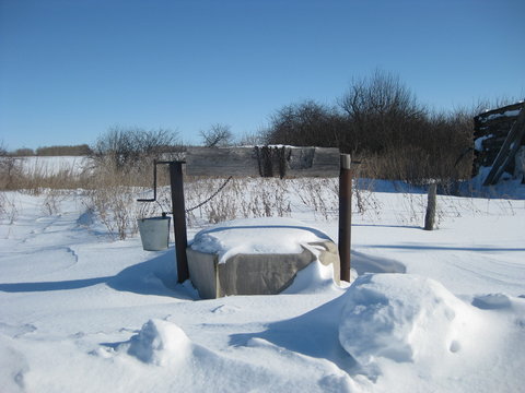 Old well. On the handle hangs a bucket. Bucket on a chain, with which you can get water. Winter landscape.  All covered with snow. - Powered by Adobe