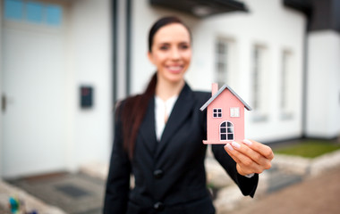 Real estate agent with model of house in front of home for sale, copy space