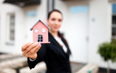 Real estate agent with model of house in front of home for sale, copy space