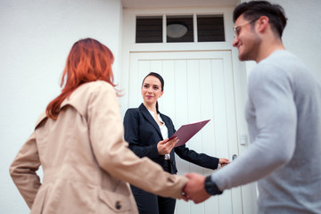 Real estate agent near door inviting young couple to enter house for visit