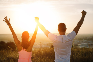 Back view of couple young of athletes with arms up towards the sunset. Sporty man and woman...