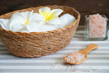 Fototapeta na wymiar Close up topview himalayan pink salt in the spoon and white towel in the basket decorate with white flower on spa table.