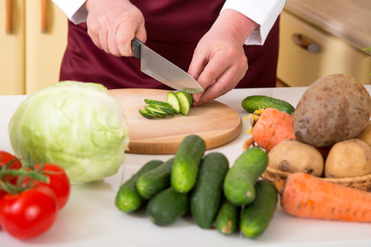 Preparation of vegetable salad. Close-up of a man's hand with a knife chopped cucumber.