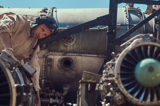 Portrait of a mechanic in uniform and flying helmet, repairing the dismantled airplane turbine in an open-air museum.