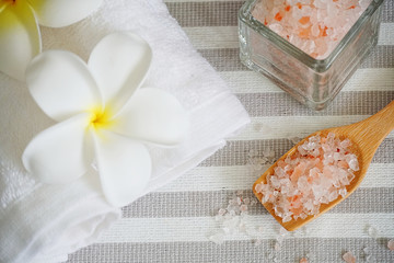 Obraz na płótnie Canvas Close up topview himalayan pink salt in the spoon and white towel decorate with white flower on spa table.