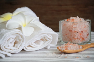 Himalayan pink salt in the spoon and white towel decorate with white flower on spa table.