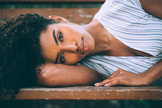 Beautiful Young Black Woman Laying Down On A Chair In A Park