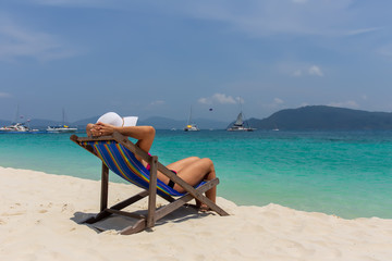 A girl in a white hat sunbathing in a deckchair and looking into