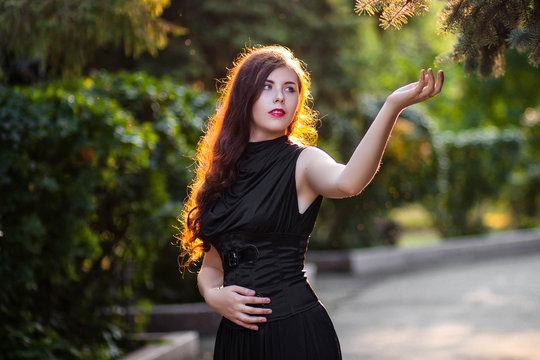 beautiful, young girl in a black dress with a corset in the park in the evening at sunset. A model with clean skin.