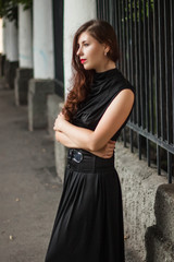 beautiful, young girl in a black dress with a corset on a background of a fence with clones. A model with clean skin.