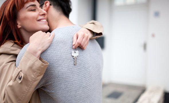 Happy couple with keys hugging in front of their new home after buying real estate