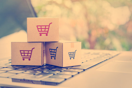 Online shopping / ecommerce and delivery service concept : Paper cartons with a shopping cart or trolley logo on a laptop keyboard, depicts customers order things from retailer sites via the internet.