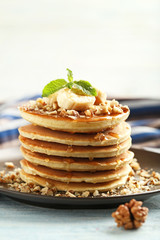 Tasty pancakes with walnuts and bananas on wooden plate