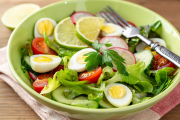Fresh salad with vegetables and quail eggs on rustic wooden background