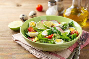 Fresh salad with vegetables and quail eggs on rustic wooden background