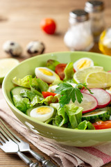 Fresh salad with vegetables and quail eggs on rustic wooden background