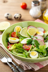 Fresh salad with vegetables and quail eggs on rustic wooden background