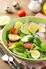 Fresh salad with vegetables and quail eggs on rustic wooden background