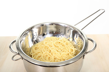 Ugotowany makaron spagetti odcedzony na metalowym durszlaku, sitku.
