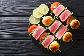Barbecue of fresh tuna, tomatoes, potatoes and green onion on skewers close-up. horizontal top view