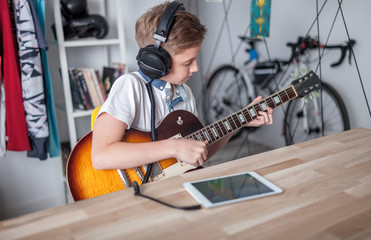 Kid boy learning to play electric guitar using tablet with headphones