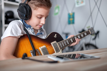 Fototapeta premium Kid boy learning to play electric guitar using tablet with headphones
