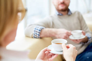 Crop blur view of persons sitting and holding cups with tea in hands