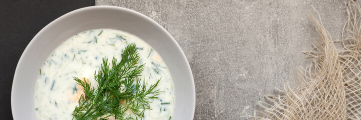 Panoramic view on a white plate with a cucumber cooler with fresh dill on a concrete counter with jute