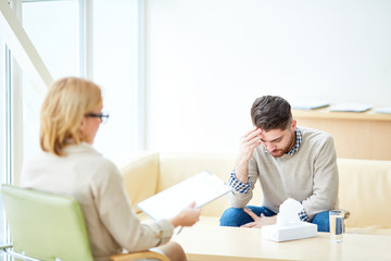 Fototapeta premium Woman with clipboard consulting young man having problems after emigration sitting in light cabinet