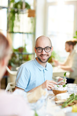 Fototapeta na wymiar Young bald male in glasses cutting vegetables for salad and smiling