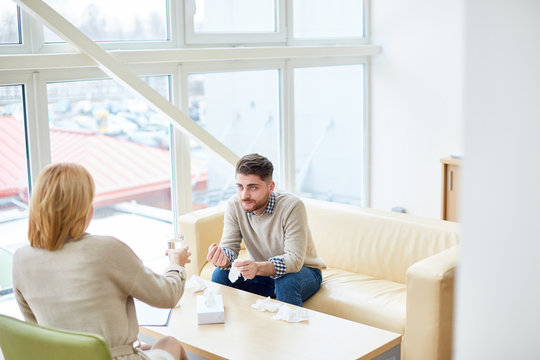 Woman working with upset man during psychotherapy and giving him glass of water