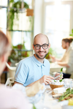 Young bald male in glasses cutting vegetables for salad and smiling