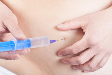 Obraz na płótnie Canvas Woman is injecting hormones to belly with syringe. IVF concept.