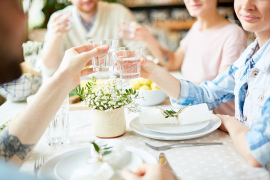 Crop Blur View Of Mates Sitting At Serving Table And Clinking Glasses With Water Celebrating Event In Cafe