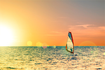 Windsurfer in the sea with a scenic sunset sky. Toned, lens sun flare. Active sport vacation concept