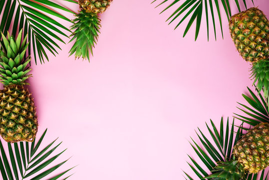 Pineapples and tropical palm leaves on punchy pastel pink background. Summer concept. Creative flat lay with copy space. Top view