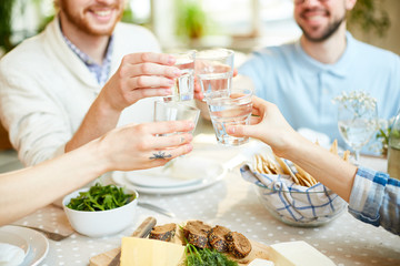 Crop blur view of friends sitting at serving table and clinking glasses with water celebrating...