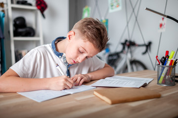 Focused preteen boy doing homework on desk in his room