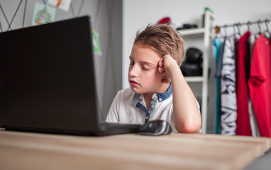 Bored sleepy preteen boy using laptop in his room at home