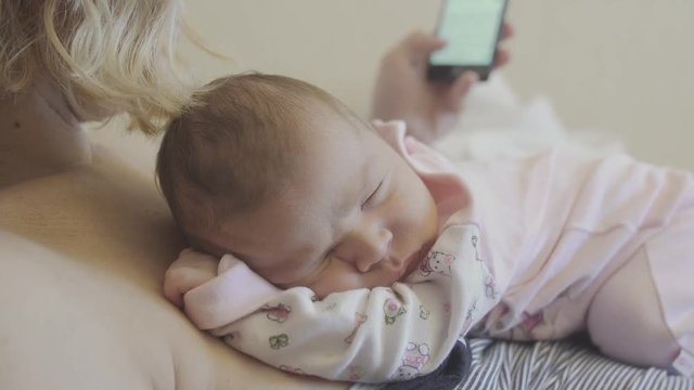 mom works on the phone and holds a newborn baby