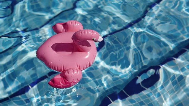 Empty inflatable flamingo floaties floating on pool water. Fun colorful floats waiting for a party on a hot summer day.