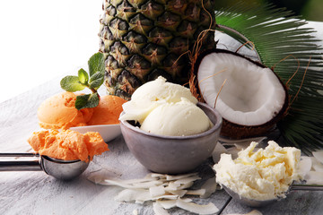 Bowl with balls of coconut ice cream and pineapple ice cream and desiccated coconut on wooden table