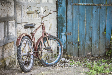 Fototapeta na wymiar Old rusty children's bike near a blue door in the garden