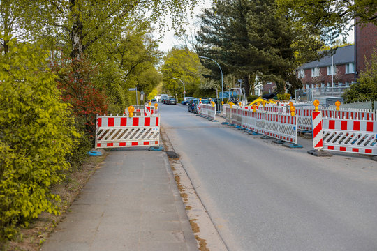 Baustelle an einem Fu&szlig;g&auml;ngerweg, mit orangenen Warnlampen beleuchtete Barrikaden blockieren den Gehweg