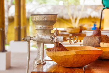 Close up of cacao beans and cacao milled over a wooden table, with hand mill, in a blurred background
