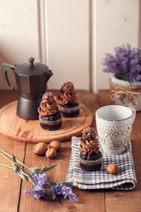Tasty chocolate cupcakes on wooden board. Cup of coffee. Geyser coffee maker. Violet flowers
