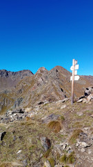 Fototapeta premium Crossroad signpost on a mountain peak at the end of an hiking path (Italian Alps landscape). Photo taken in a sunny summer day. Clear blue sky in the background. 